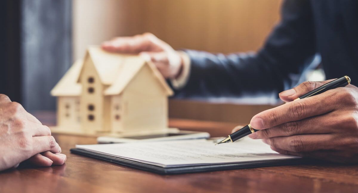 A man is signing a document in front of a model house.