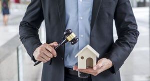 A man in a suit is holding a gavel and a model house.