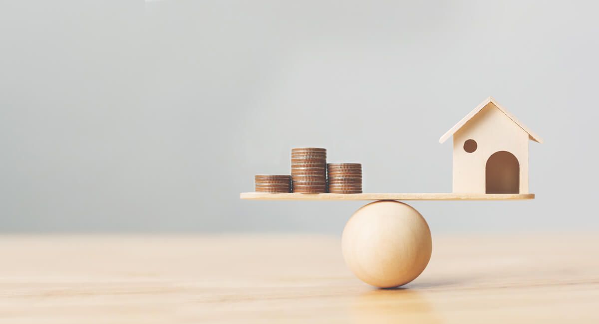 A scale with a house and stacks of coins on it.