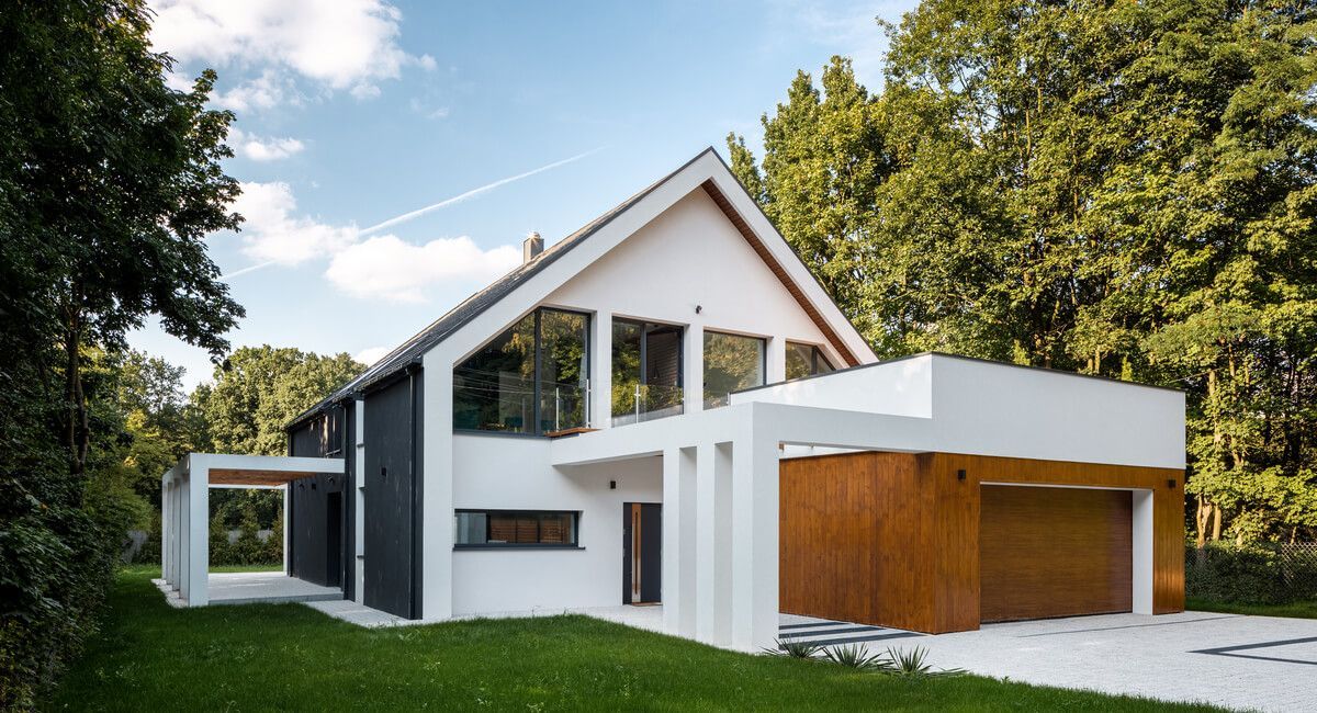 A large white house with a wooden garage door is surrounded by trees.