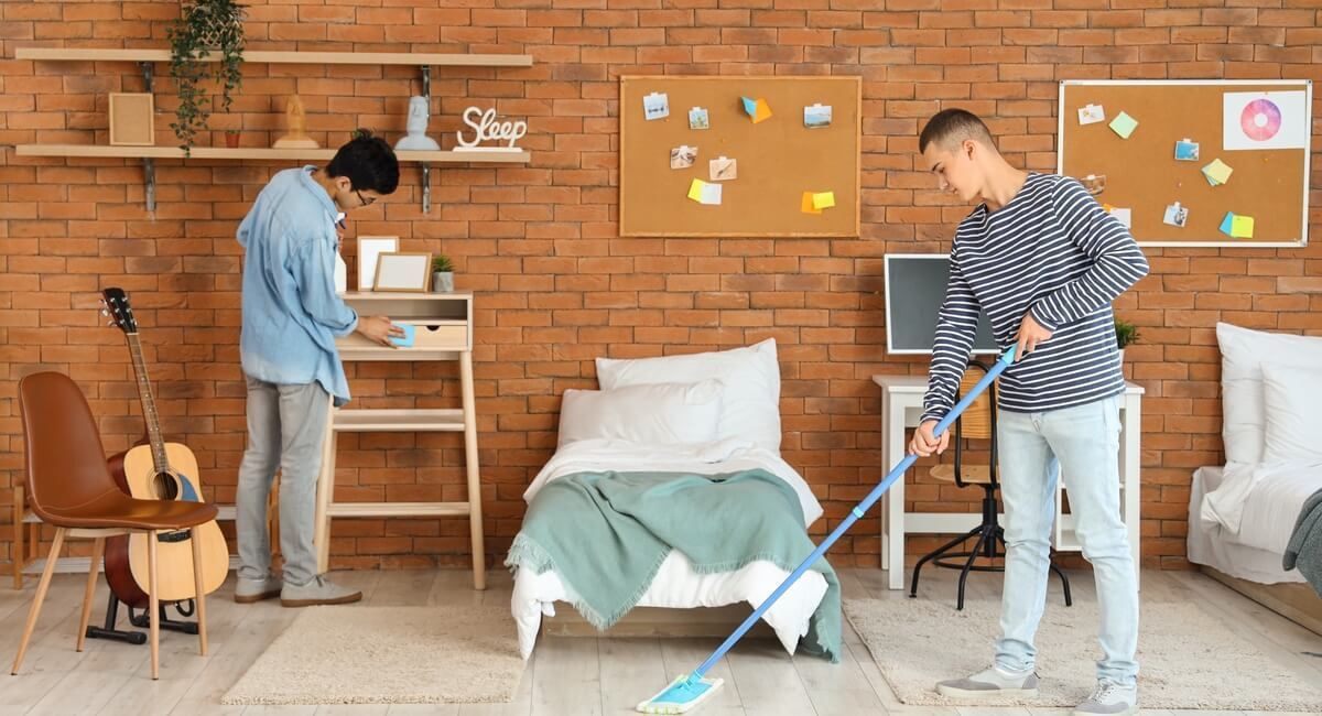 Two men are cleaning a bedroom with a mop.