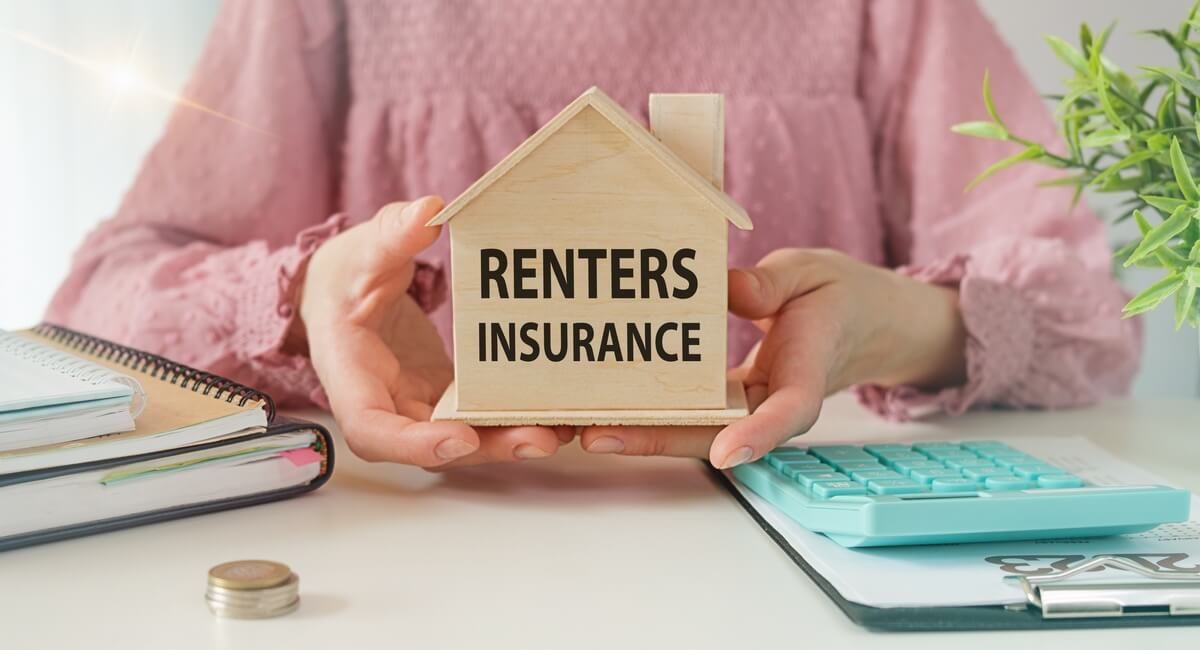 A woman is holding a small wooden house with the words `` renters insurance '' written on it.