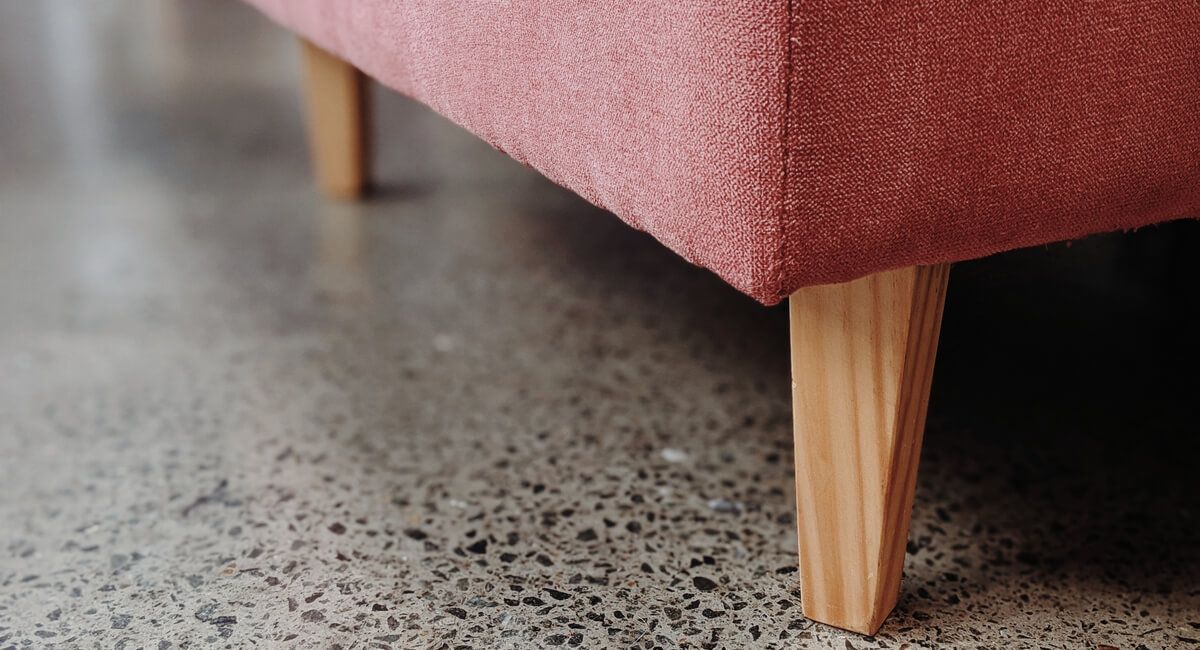 A pink couch with wooden legs is sitting on a concrete floor.