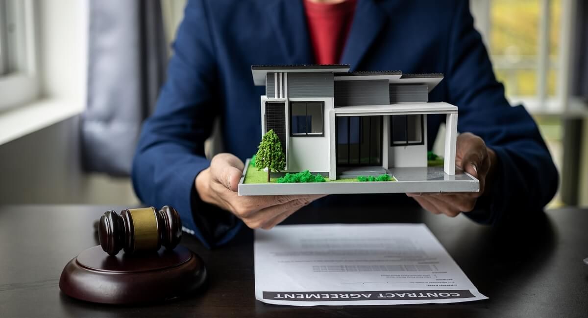 A man in a suit is holding a model house in his hands.