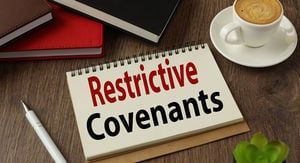 A notebook with the words restrictive covenants written on it is sitting on a wooden table next to a cup of coffee.