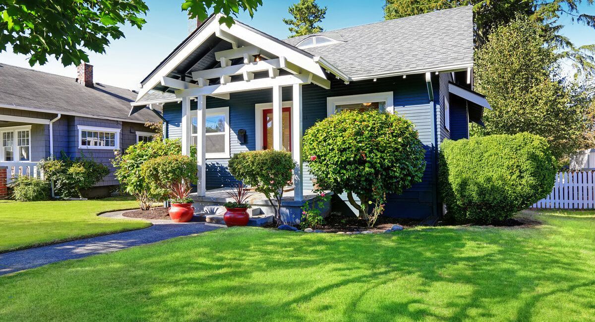 A blue house with a white porch and a lush green lawn.