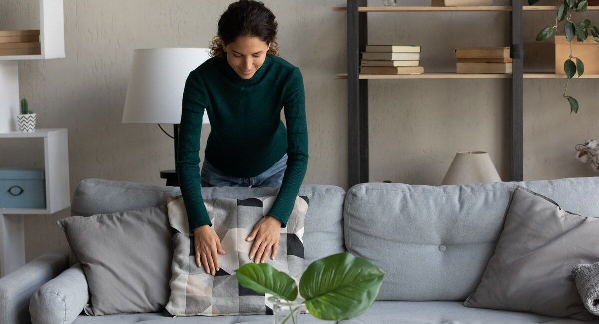 A woman is putting a pillow on a couch in a living room.