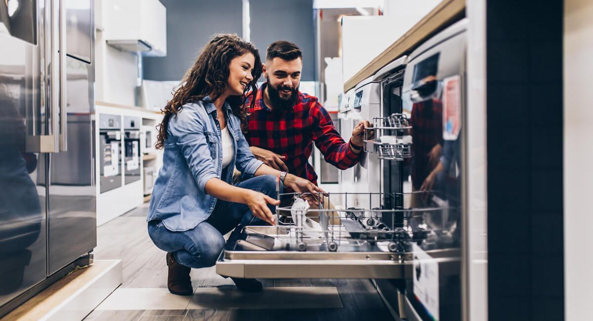 A man and a woman are looking at a dishwasher in a kitchen.