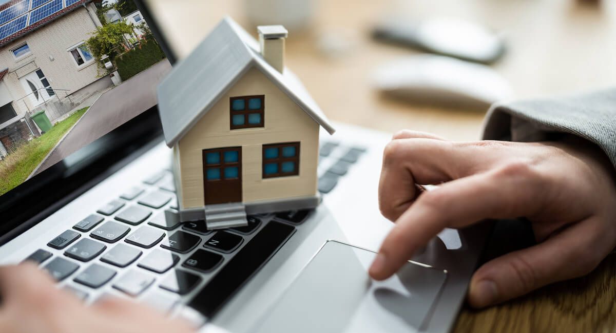 A person is typing on a laptop with a small house on the keyboard.