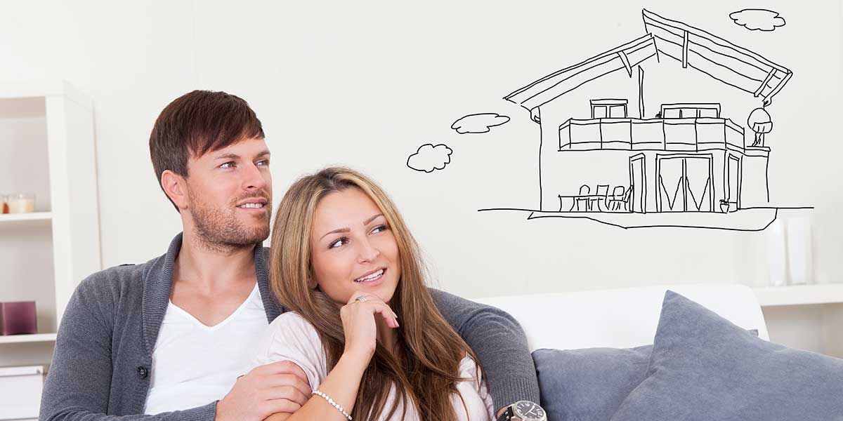 A man and a woman are sitting on a couch looking at a drawing of a house on the wall.