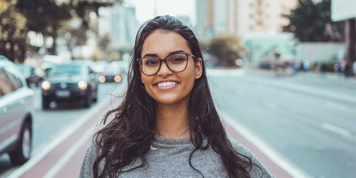 A woman wearing glasses is smiling in front of a street.