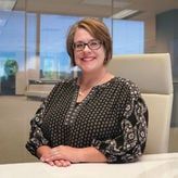 A woman wearing glasses is sitting at a desk in an office.