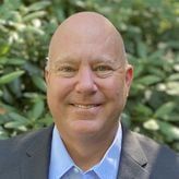 A bald man in a suit and blue shirt is smiling for the camera.