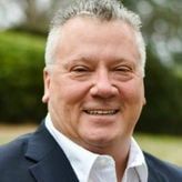 A man in a suit and white shirt is smiling for the camera.