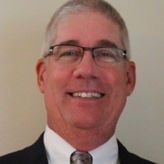 A man wearing glasses and a suit and tie is smiling for the camera.