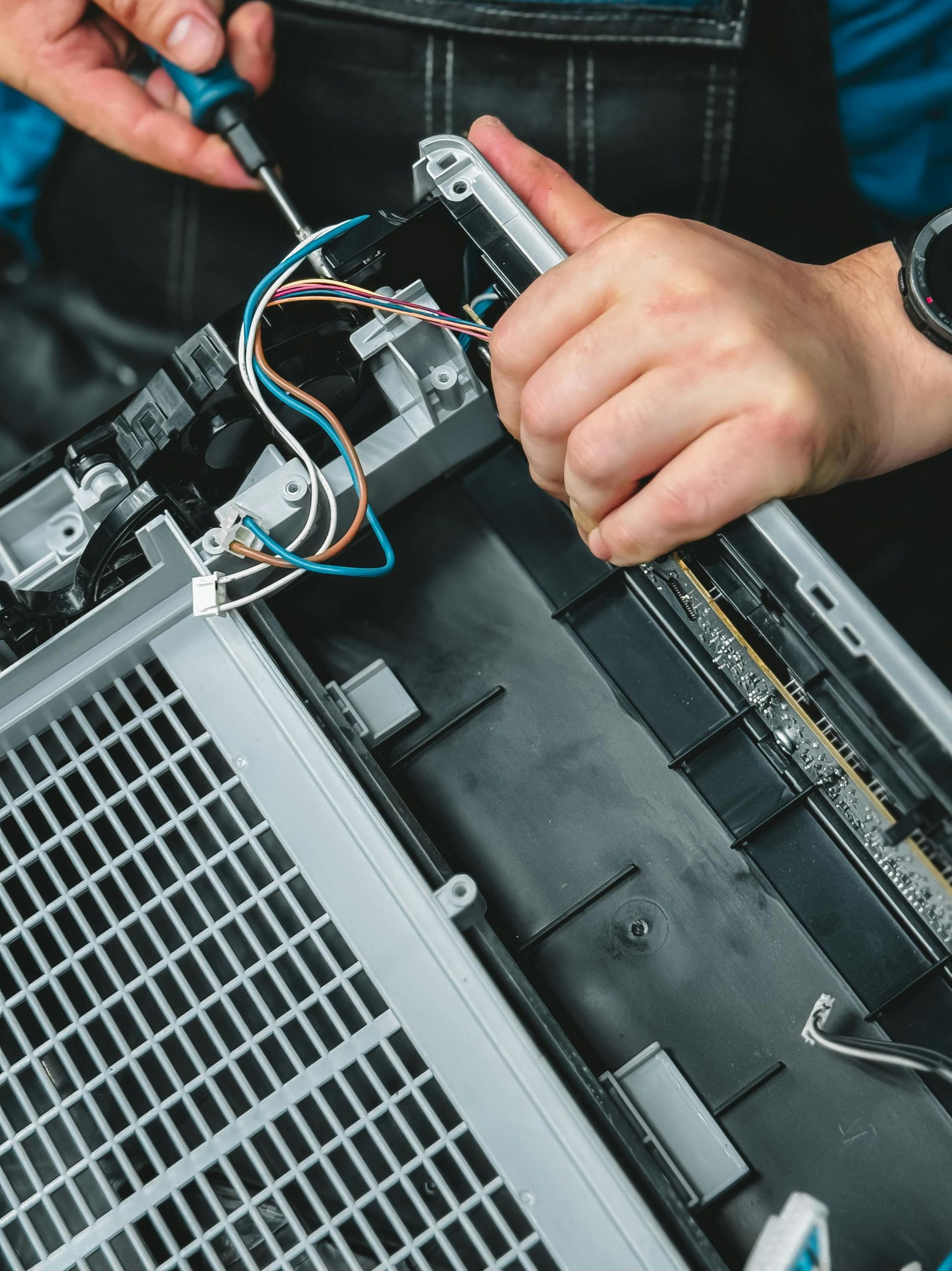 Person using a screwdriver to repair the internal components of a printer.