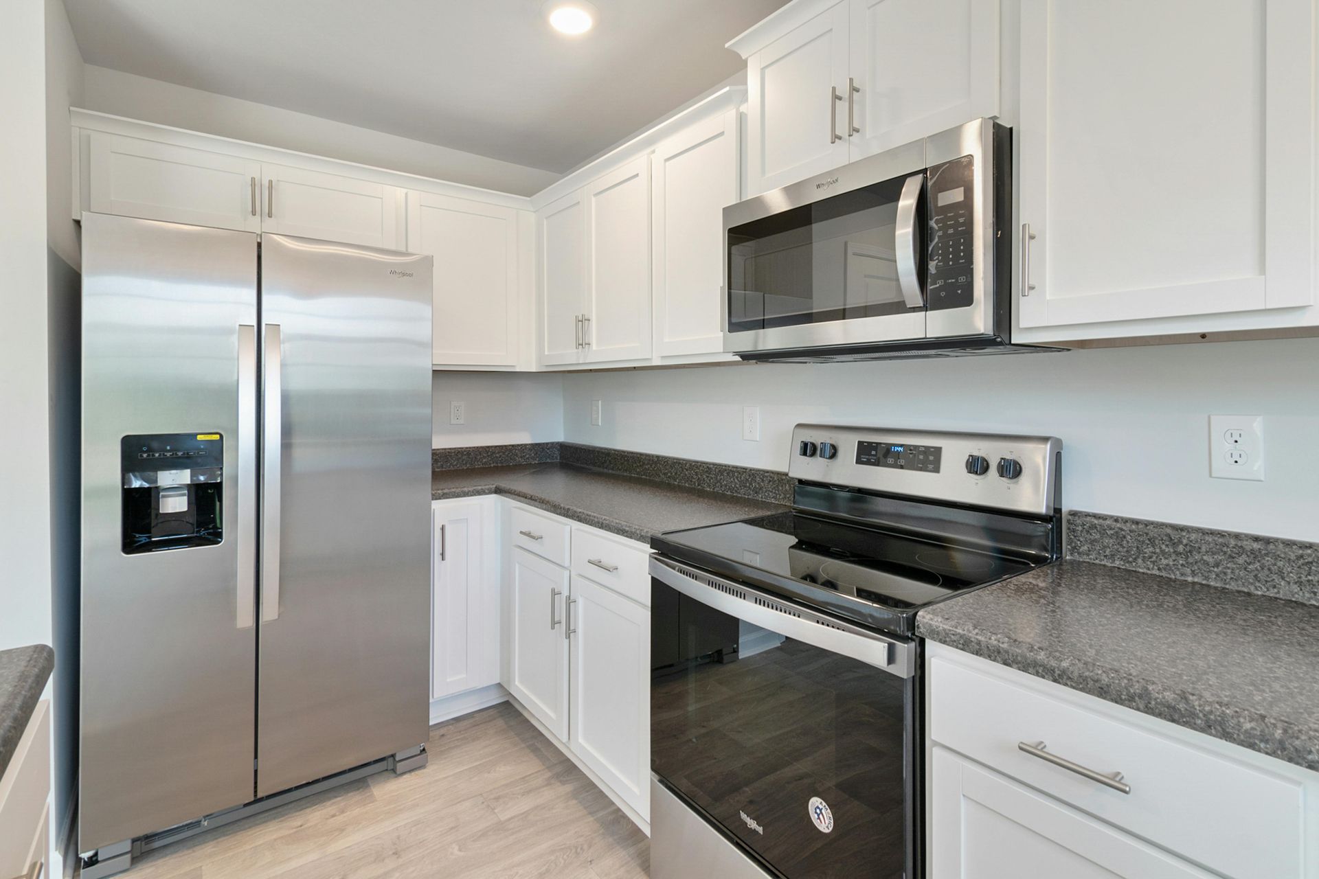 Stainless steel appliances in a bright white kitchen with gray countertops and cabinets.