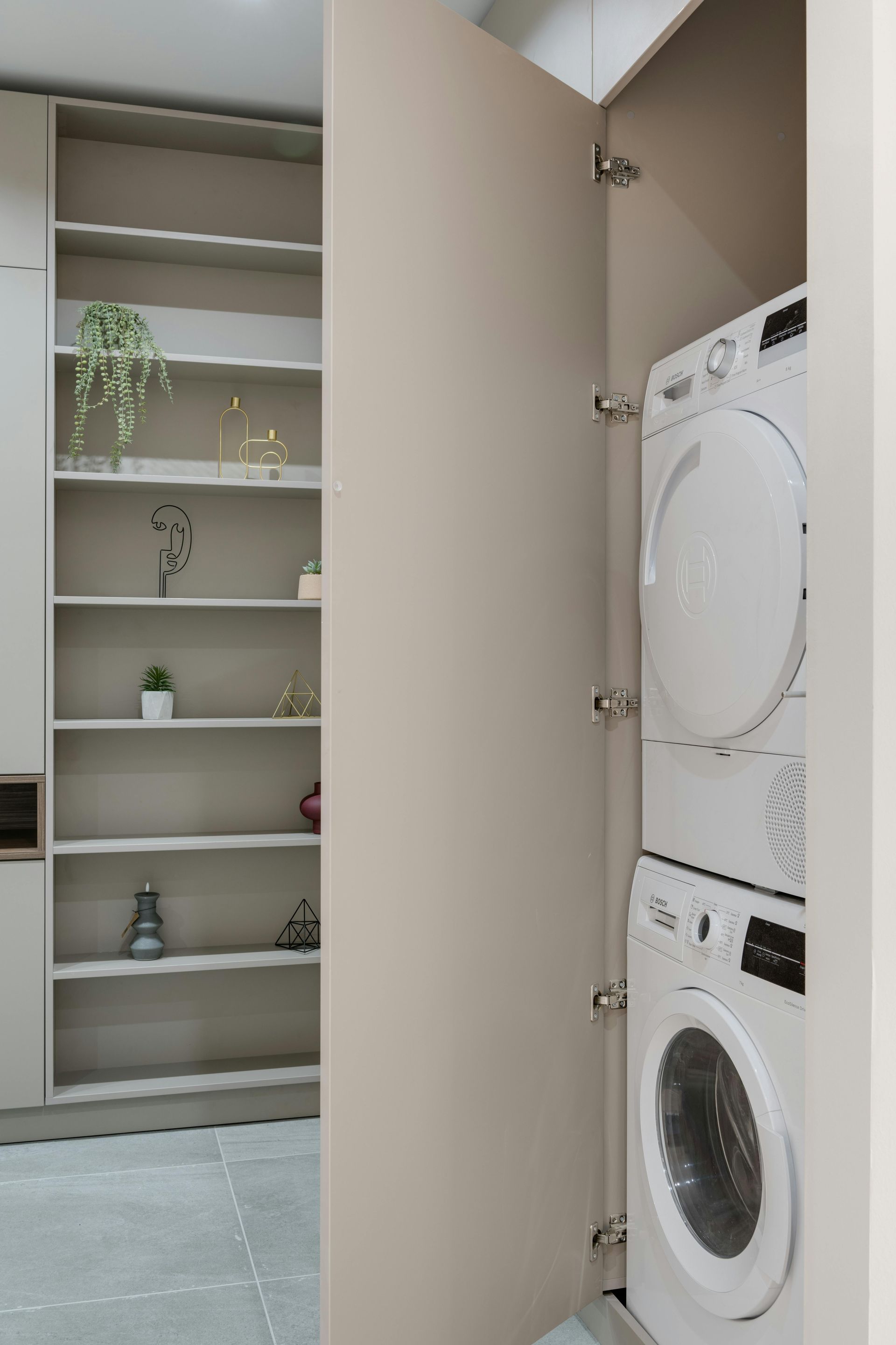 Laundry room with stacked washer and dryer behind an open door, next to shelving.