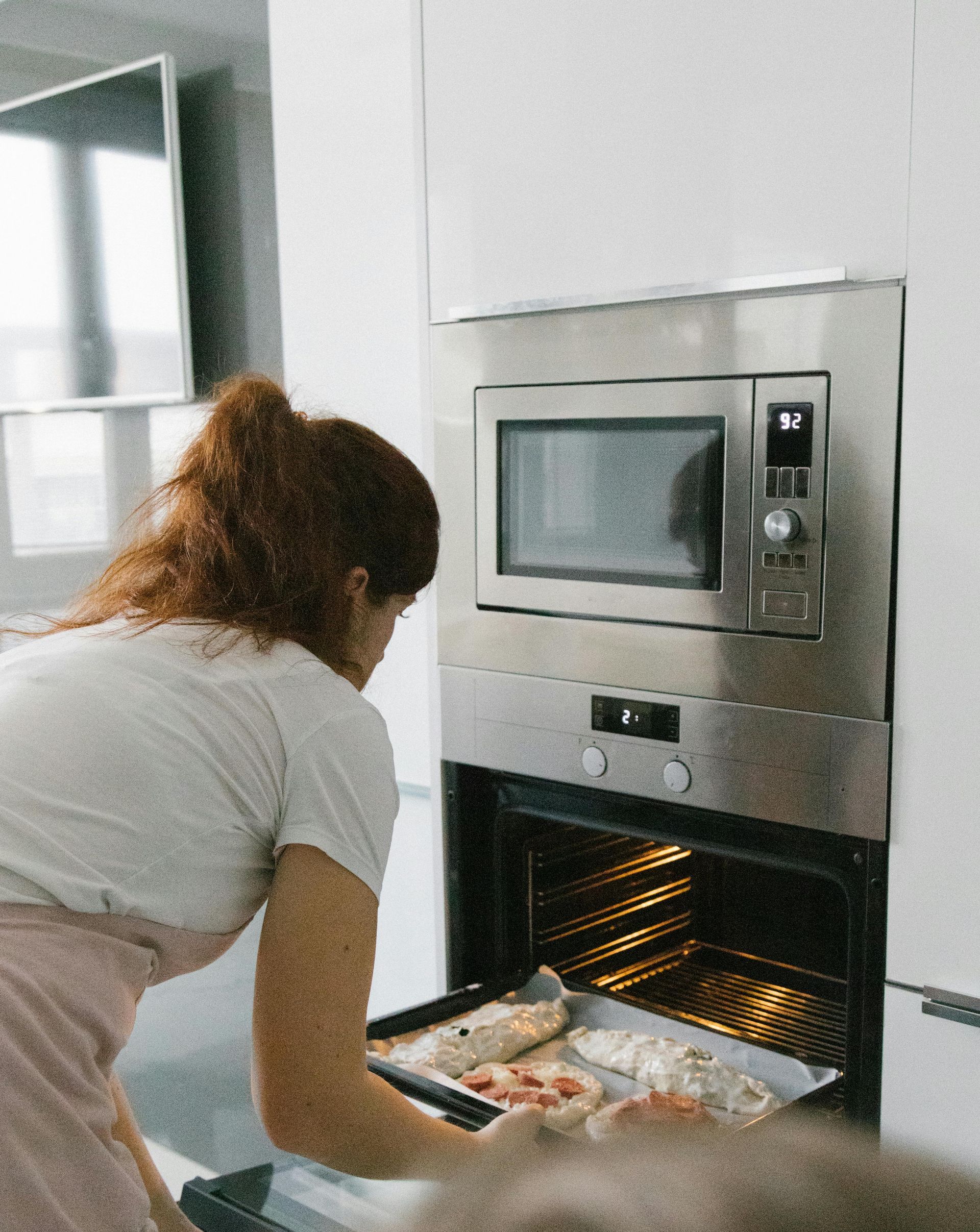 Woman in apron taking a baking sheet out of a stainless steel oven.