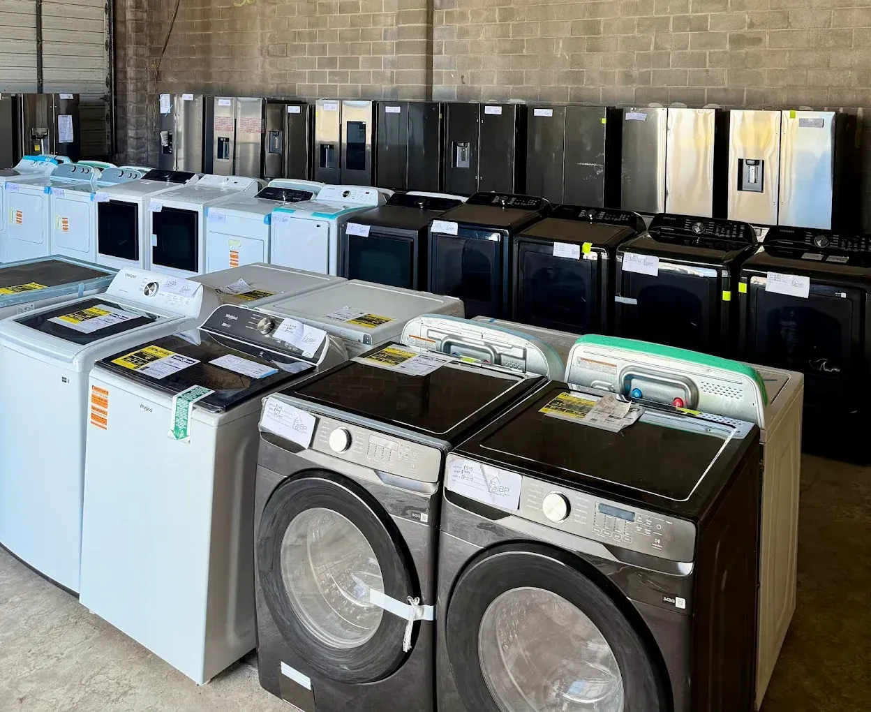 Appliances for sale in a warehouse; various washers and refrigerators in black and white.