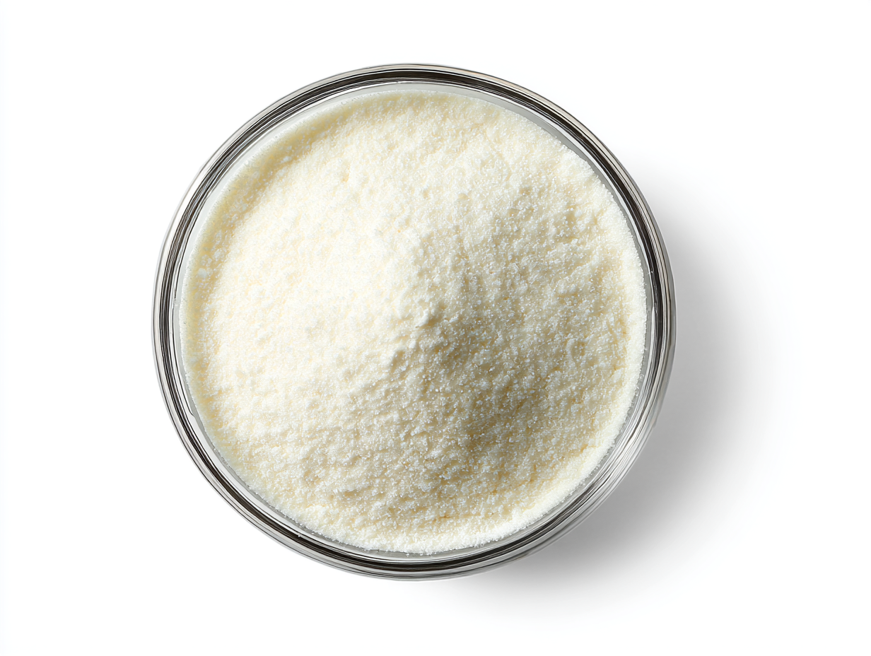 A top-down view of a glass bowl filled with white powder, likely a food ingredient, on a white surface.
