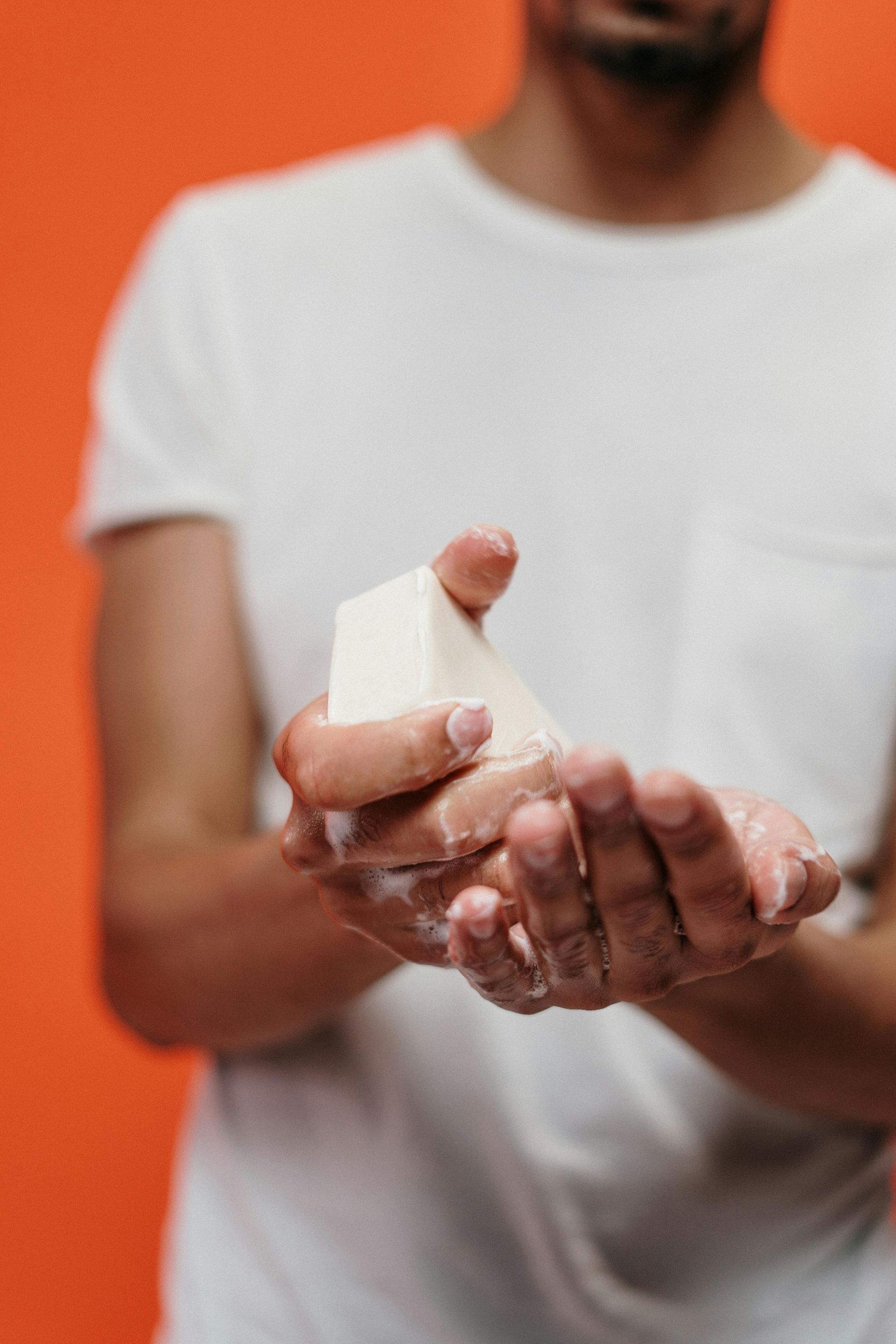 Person holding a bar of soap over sudsy hands, orange background.