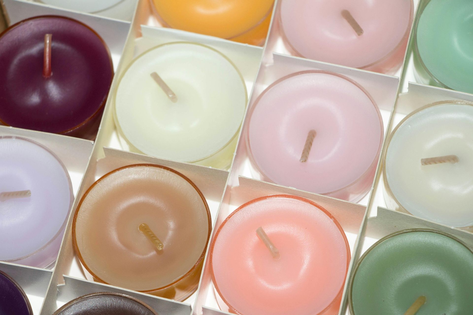 A box of colorful tea light candles, including purple, yellow, pink, and green, in a close-up view.