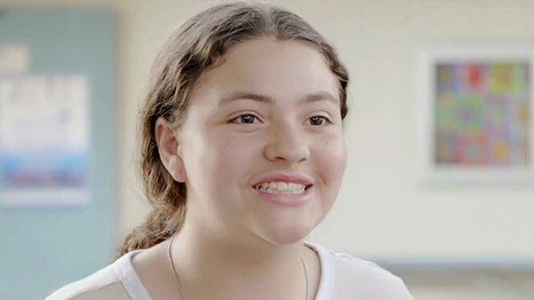 A young girl is smiling for the camera in a hallway.