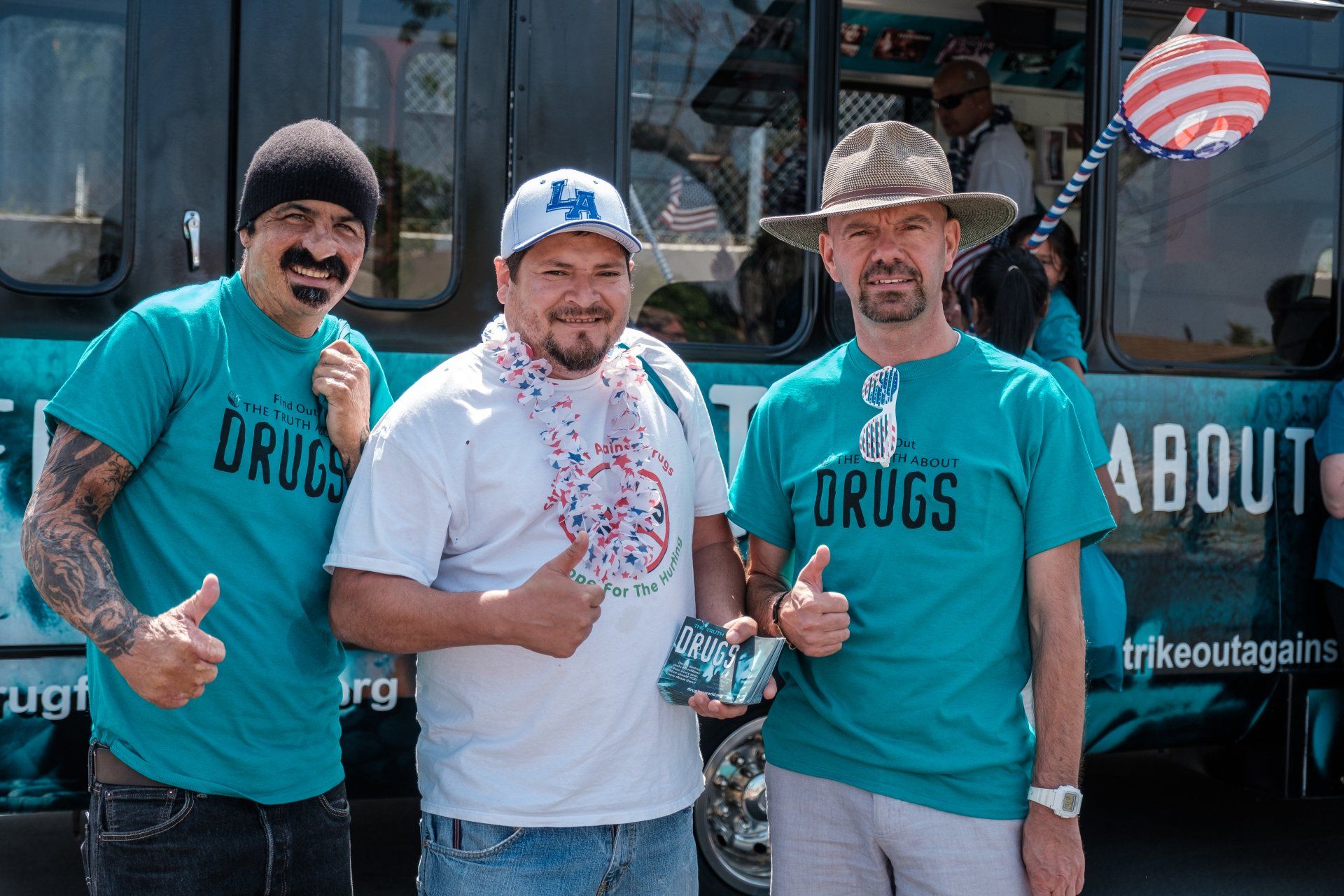 Three men are posing for a picture in front of a bus that says about drugs.