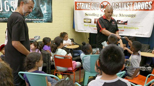 A group of children are sitting in front of a sign that says strike out against drugs