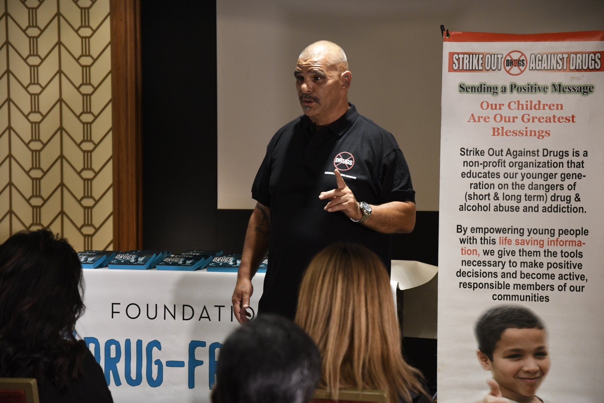A man is giving a presentation in front of a sign that says drug-free