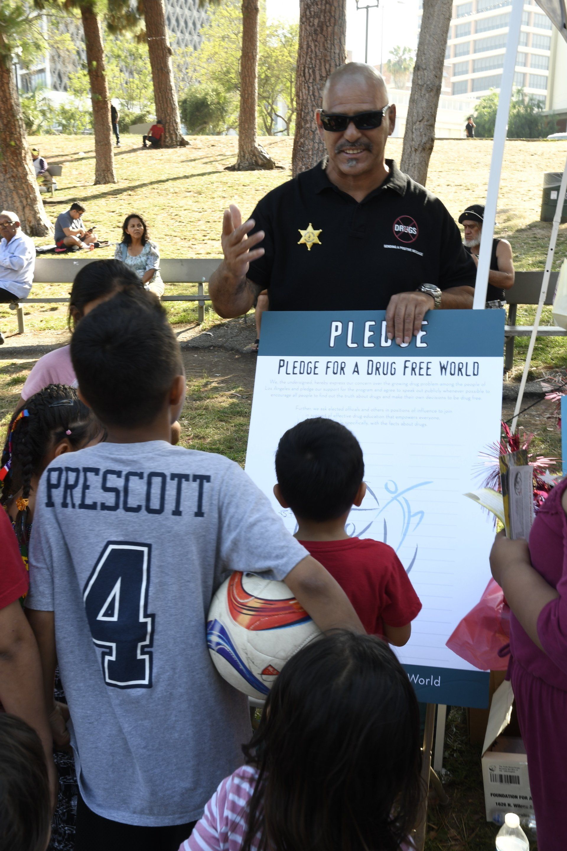 A man is standing in front of a group of children holding a sign that says pledge.
