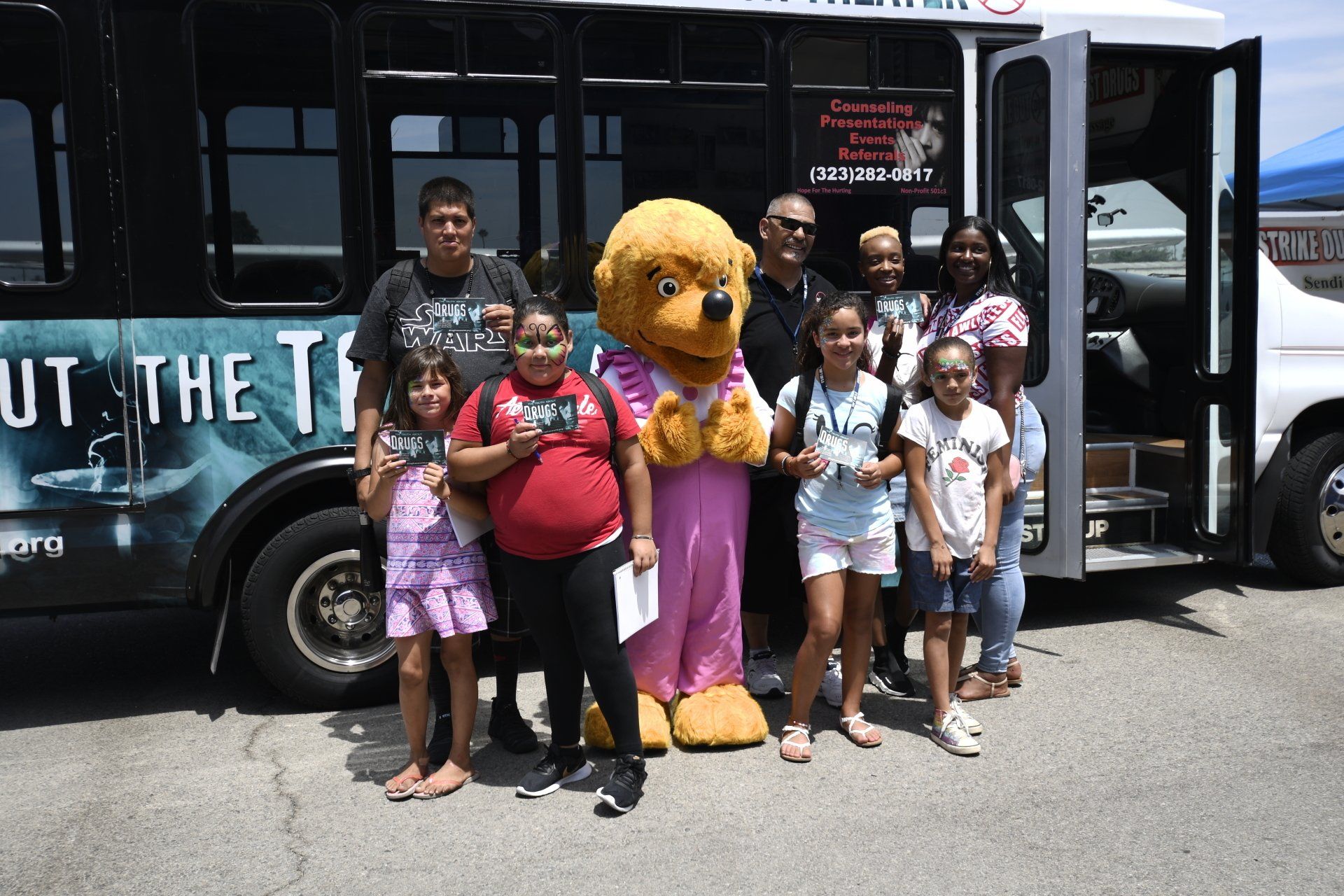 A group of people standing in front of a bus with a mascot in front of it.