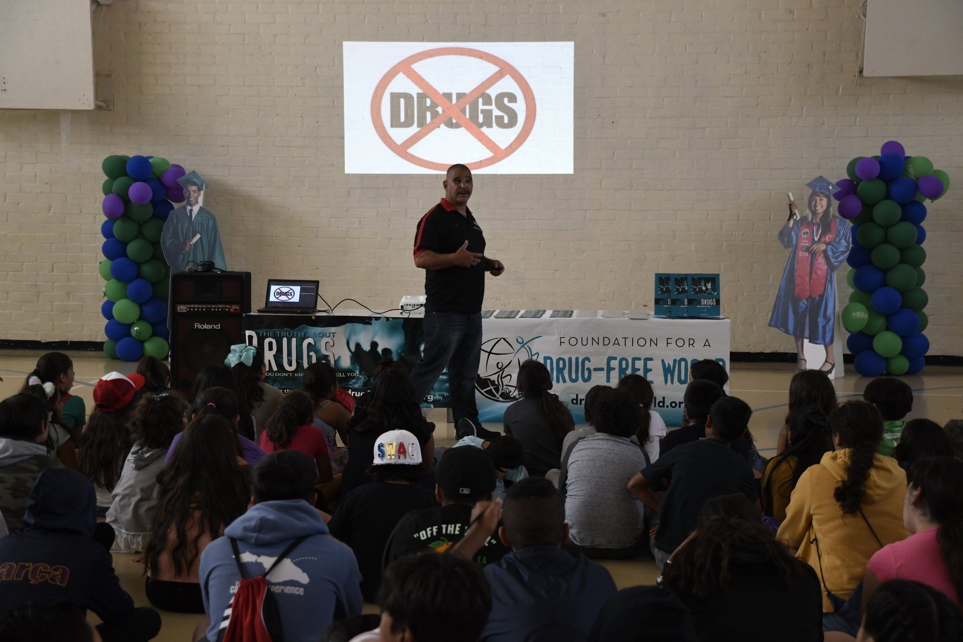 A man is giving a presentation to a group of people in front of a sign that says drugs