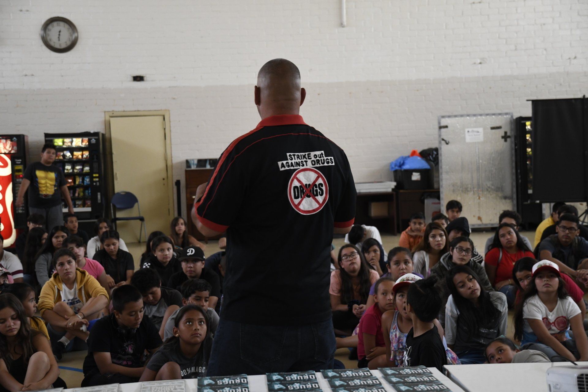 A man is giving a presentation to a group of children in a gym.