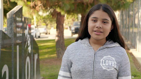 A young girl is standing in front of a sign in a park.