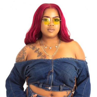 A woman with red hair is wearing sunglasses and a denim top