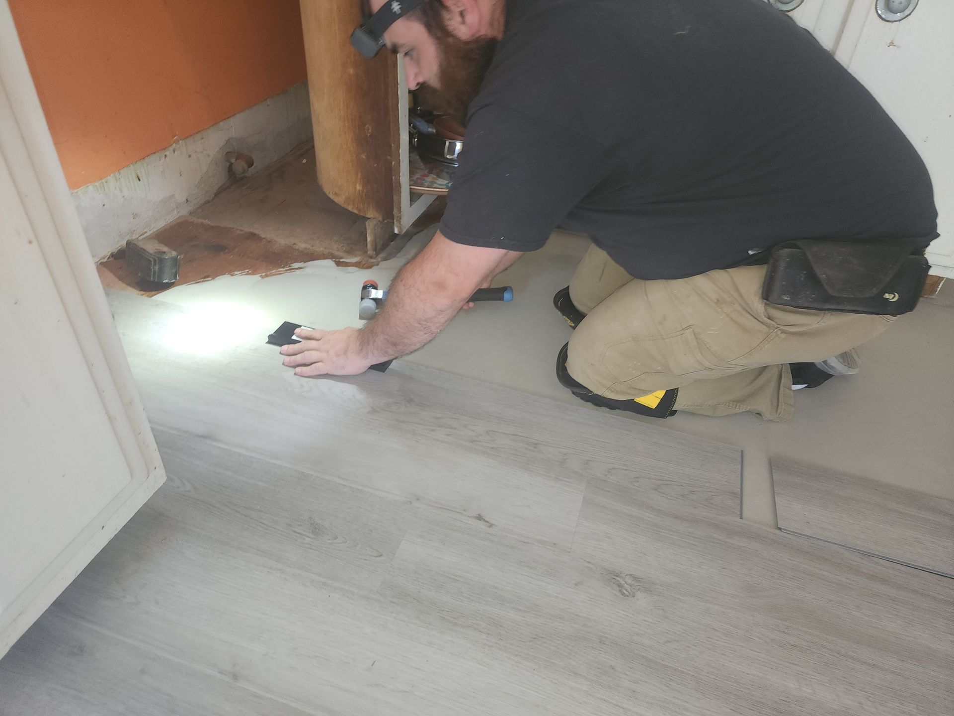 A man is kneeling down on the floor with a flashlight.