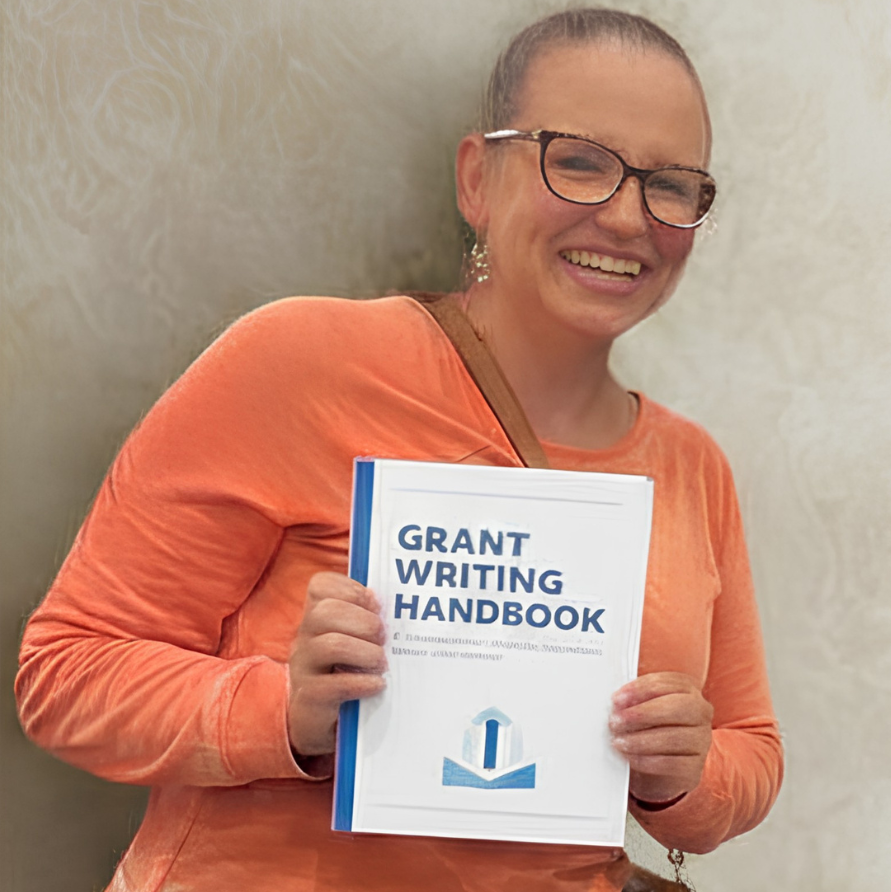 Smiling person in an orange shirt holding a grant writing handbook against a light background