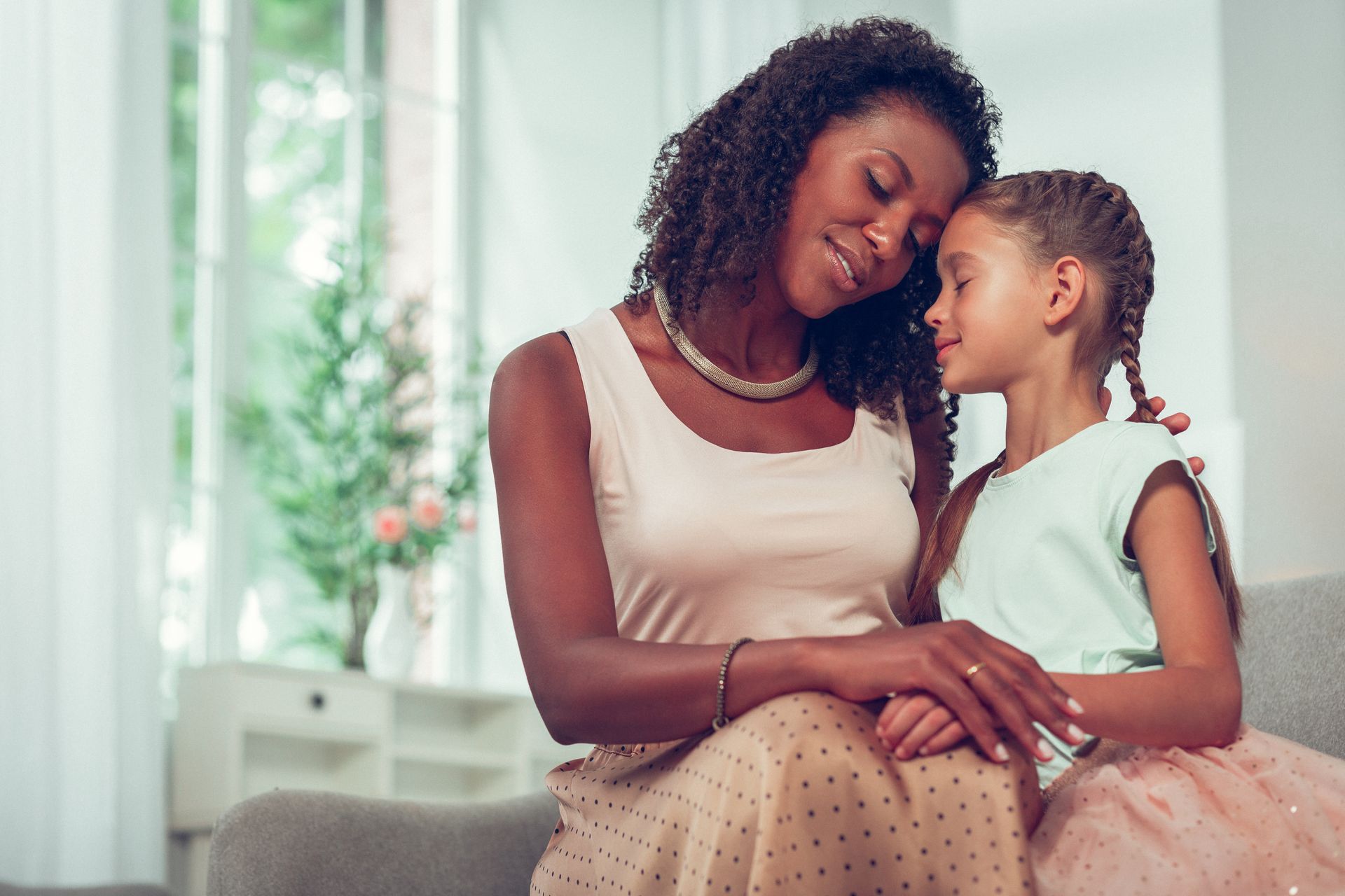 A woman and a little girl are sitting on a couch and hugging each other.