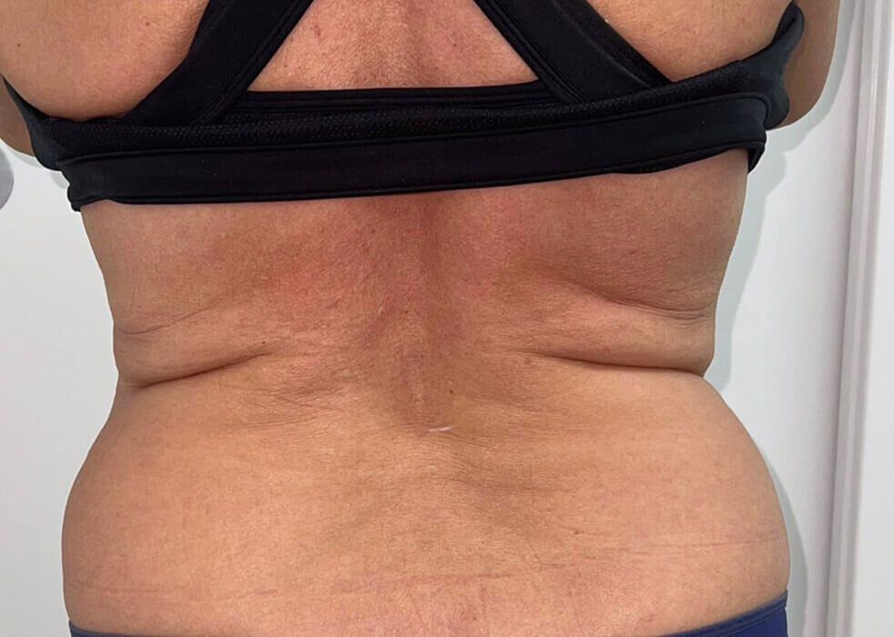 The back of a woman wearing a black sports bra and blue shorts.