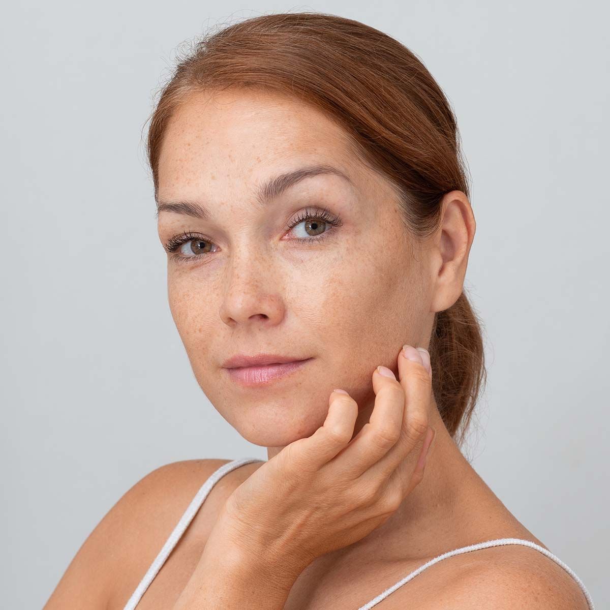 A woman is touching her face with her hand and looking at the camera.