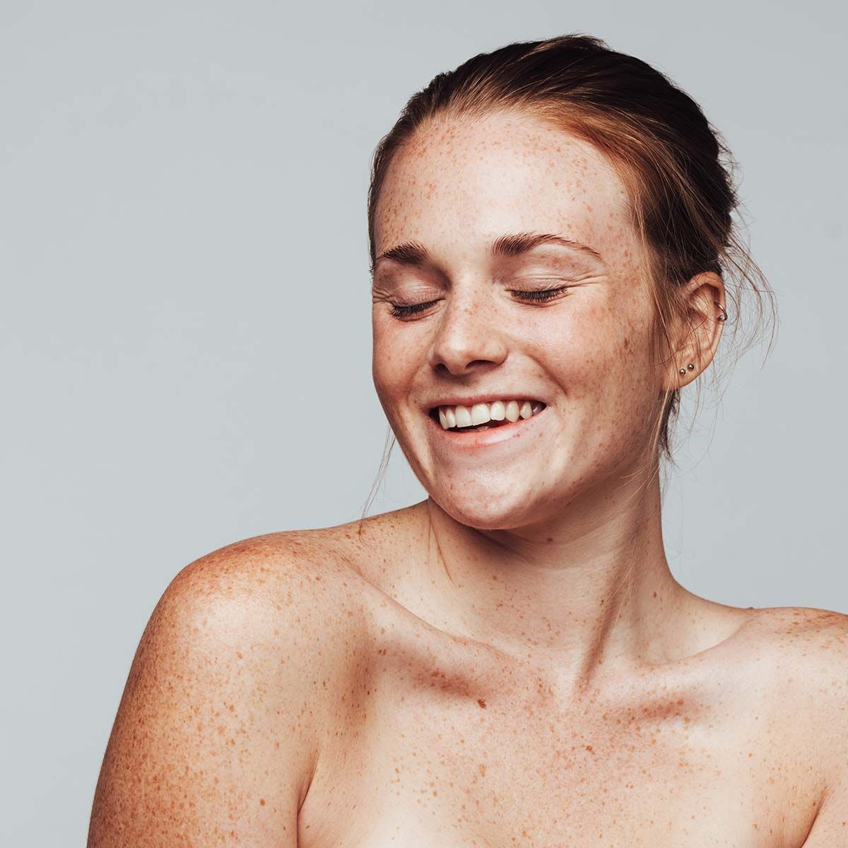 A woman without a shirt is smiling with her eyes closed.