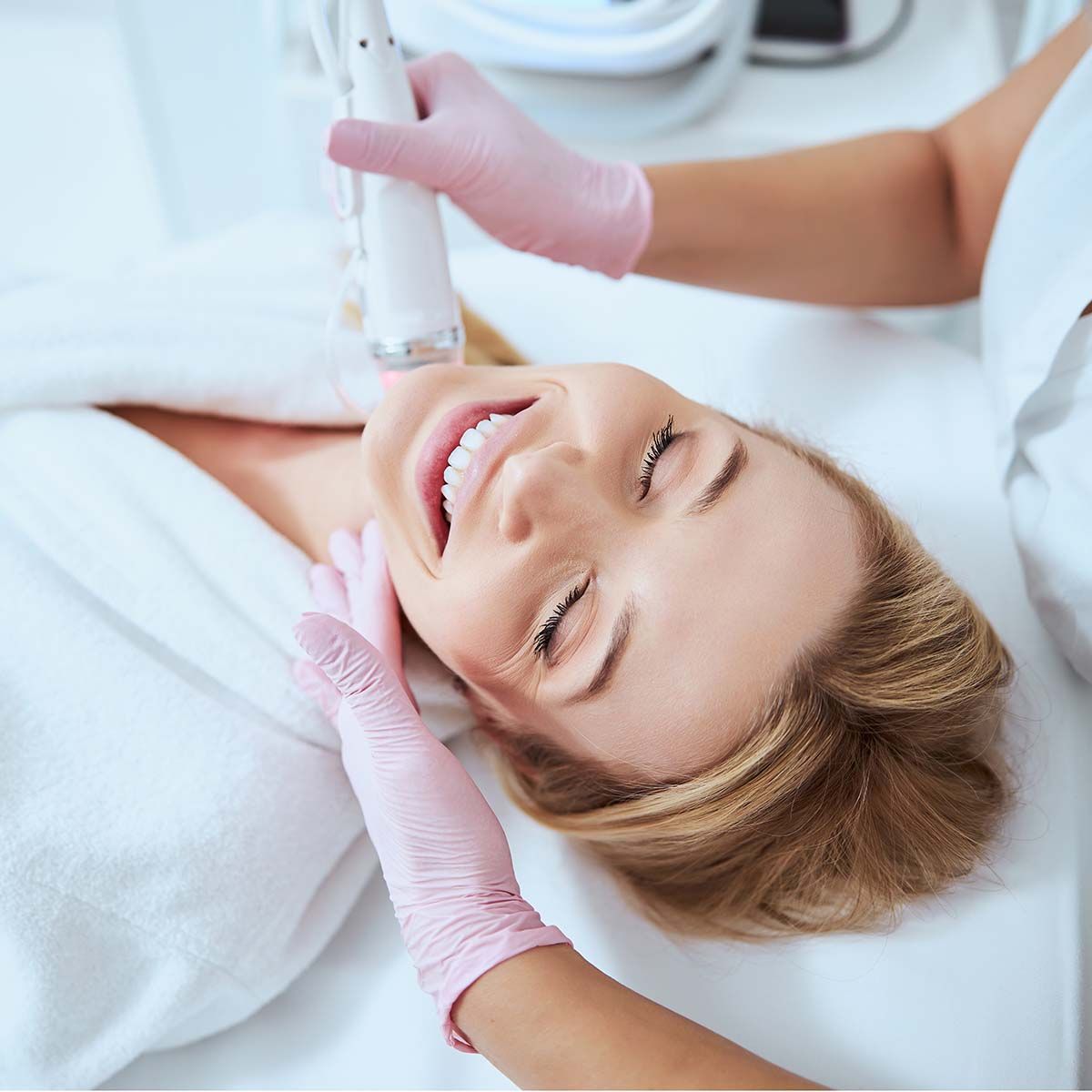 A woman is smiling while getting a facial treatment at a beauty salon.
