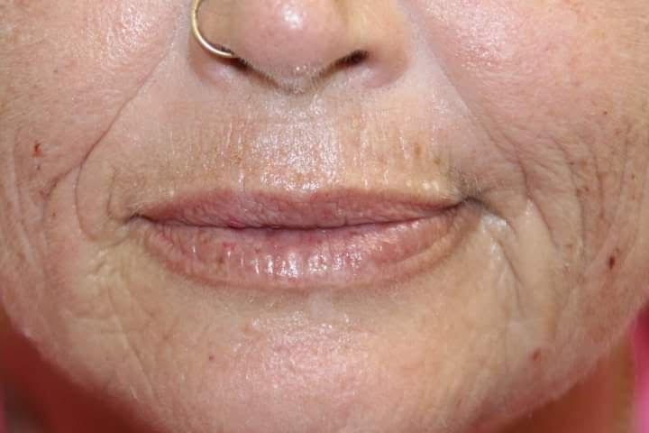 A close up of a woman 's face with wrinkles and a nose ring.