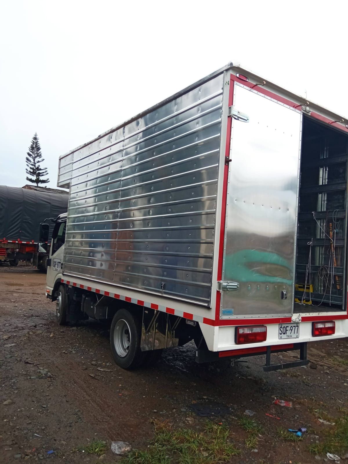 Una camioneta plateada con la puerta abierta está estacionada en un lote de tierra.