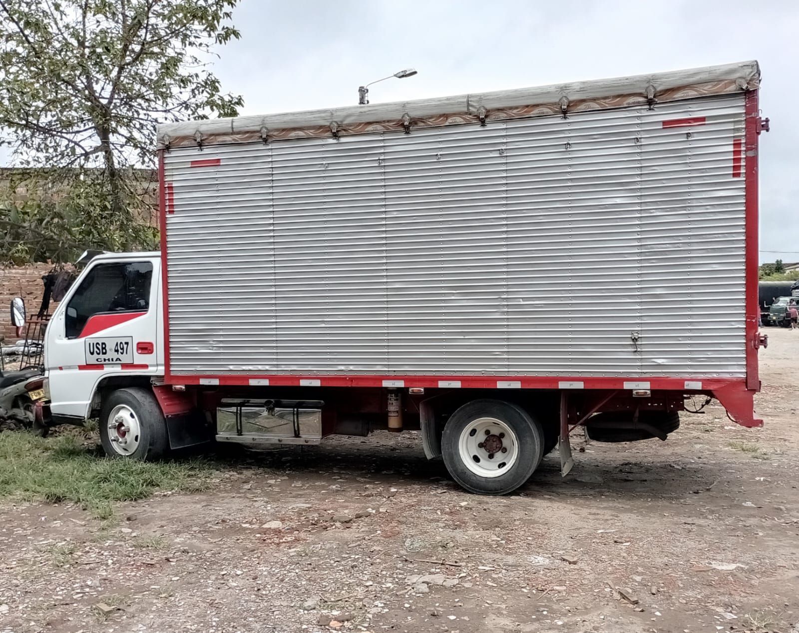 Un camión plateado y rojo está estacionado en un lote de tierra.