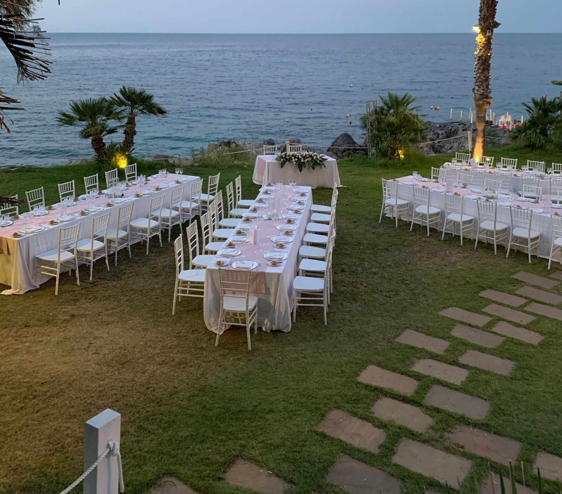 Allestimento per ricevimento di nozze con tavoli e sedie sull'erba con vista sull'oceano.