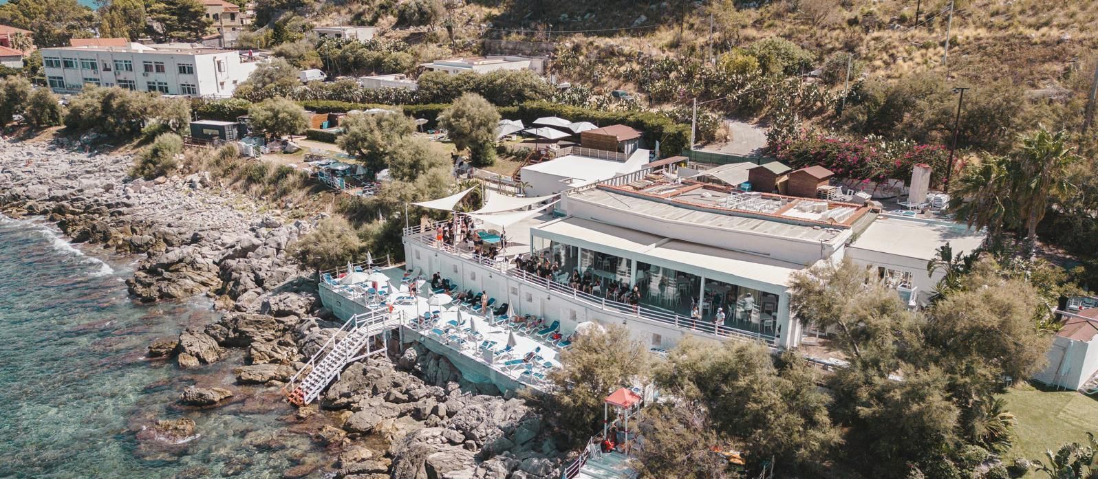 Località costiera con edifici bianchi, acqua azzurra e costa rocciosa.