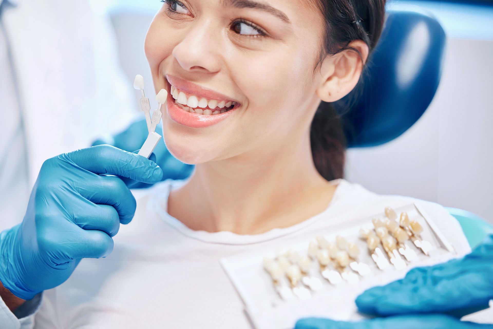 Smiling woman in dental chair as dentist matches tooth shade with veneer color chart. Smiling woman in dental chair as dentist matches tooth shade with veneer color chart.